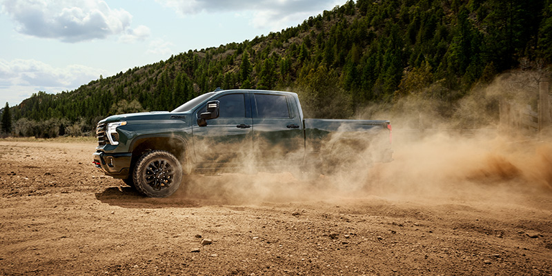 Green Chevrolet Silverado pickup truck kicking up dust while driving off-road in a forested area.
