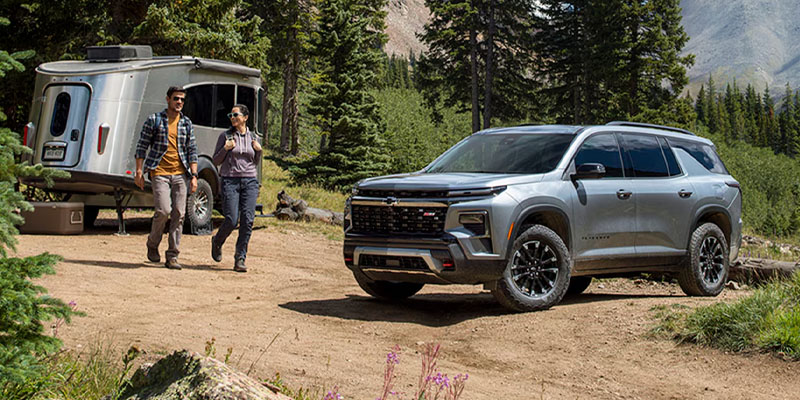 Silver Chevrolet SUV with camper trailer on a forest trail.